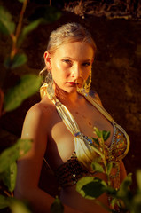 A beautiful young woman glitters golden in the
evening sunlight. She is seen relaxing between 
large rocks in a stone quarry. 
