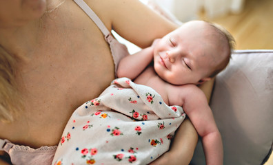 Young mother holding her newborn baby child sit on a chair in the living room. Close view on the baby