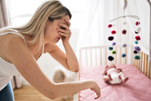 Mother Suffering From Postnatal Depression Near Crib With Cute Baby At Home