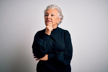 Senior beautiful woman wearing casual black sweater standing over isolated white background with hand on chin thinking about question, pensive expression. Smiling with thoughtful face. Doubt concept.