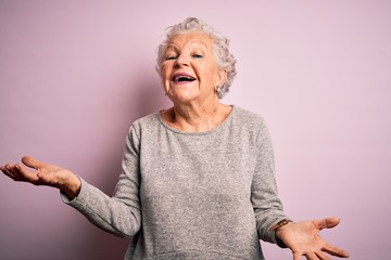 Senior beautiful woman wearing casual t-shirt standing over isolated pink background smiling cheerful with open arms as friendly welcome, positive and confident greetings