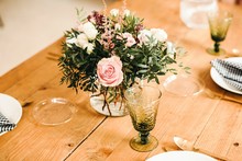 From Above Bouquet Of Miscellaneous Flowers And Green Plant Twigs In Vase With Water On A Wooden Table Set For A Meal