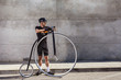 © Macia Puiggros/ADDICTIVE STOCK - Calm determined man in black activewear and helmet looking away while standing on asphalt road and leaning on high wheel bicycle against concrete wall in sunny day