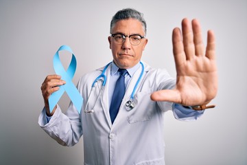 Poster - Middle age handsome grey-haired doctor man wearing coat holding blue cancer ribbon with open hand doing stop sign with serious and confident expression, defense gesture