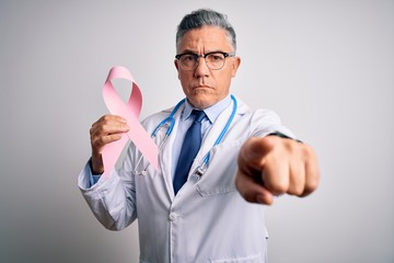 Poster - Middle age handsome grey-haired doctor man holding pink cancer ribbon pointing with finger to the camera and to you, hand sign, positive and confident gesture from the front