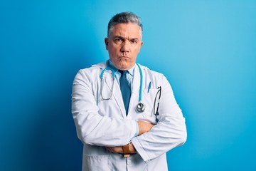 Poster - Middle age handsome grey-haired doctor man wearing coat and blue stethoscope skeptic and nervous, disapproving expression on face with crossed arms. Negative person.