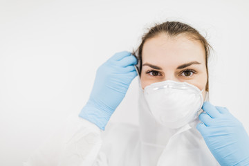 The girl doctor puts on a white protective medical mask in blue gloves on a white background.