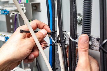 Hands fasten the cable ties on the cable, which are on the cable tray. Close-up. Horizontal orientation.