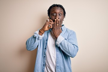 Canvas Print - African american man having conversation talking on the smartphone over white background cover mouth with hand shocked with shame for mistake, expression of fear, scared in silence, secret concept