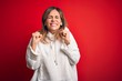 © Krakenimages.com - Middle age beautiful sportswoman wearing casual sweatshirt over isolated red background excited for success with arms raised and eyes closed celebrating victory smiling. Winner concept.