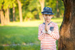 © Chendekova Liudmila - A young boy in a hat stands in the garden near the trees and looks straight. Close-up portrait.