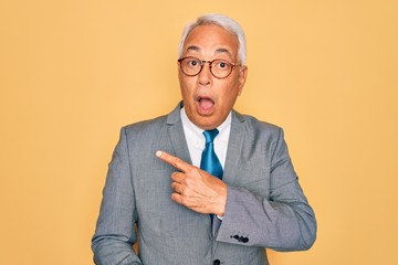 Sticker - Middle age senior grey-haired handsome business man wearing glasses over yellow background Surprised pointing with finger to the side, open mouth amazed expression.