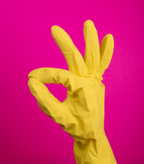 Hand with yellow rubber protective glove isolated on pink gesturing ok, okay, positive. Signs of gestures (language), gloves cleaning, kitchen gloves.
