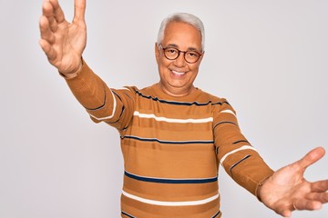 Canvas Print - Middle age senior grey-haired handsome man wearing glasses and casual striped sweater looking at the camera smiling with open arms for hug. Cheerful expression embracing happiness.