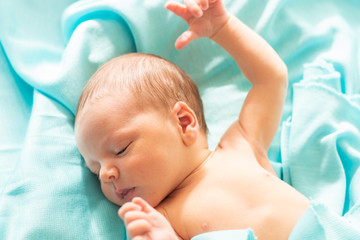 Little caucasian newborn baby falls asleep on blue, delicate and soft blanket. Baby relaxing in safe and calm atmosphere.