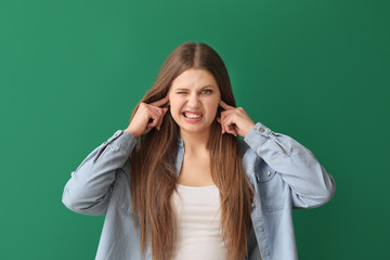 Canvas Print - Young woman suffering from loud noise on color background