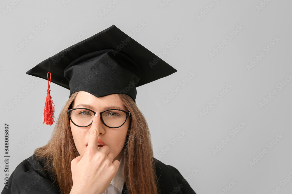 Female student in graduation hat on light background