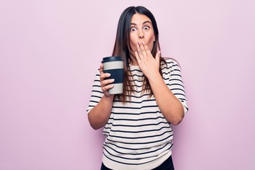 Canvas Print - Young beautiful brunette woman drinking cup of takeaway coffee over isolated pink background covering mouth with hand, shocked and afraid for mistake. Surprised expression