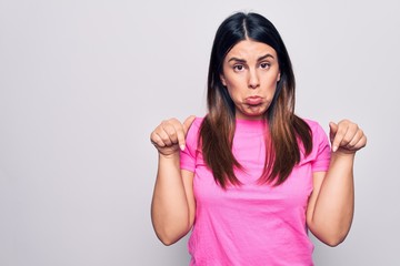 Sticker - Young beautiful brunette woman wearing casual pink t-shirt standing over white background Pointing down looking sad and upset, indicating direction with fingers, unhappy and depressed.