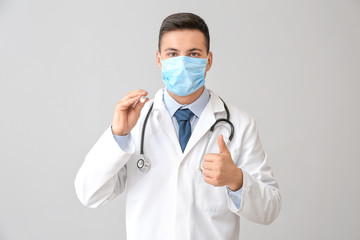 Canvas Print - Male doctor with flashlight showing thumb-up gesture on grey background