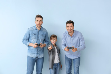 Wall Mural - Happy gay couple with adopted child playing video game on color background