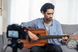 © Kawee - Asian male vlog influencer performancing music and singing show to streaming digital internet online audience listening at home. Man plays guitar and sing a song. Home entertainer and blogger concept.