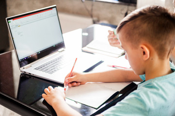 Wall Mural - The boy is studying at home. Sits at a table with textbooks, a laptop is open in front of a boy