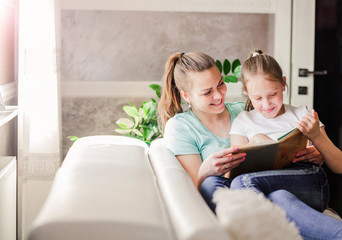 mom and daughter read a book together, a textbook sitting on a sofa at home