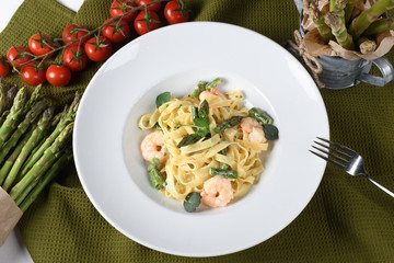 Wall Mural - Tagliatelle or pappardelle pasta with asparagus and shrimps, cherry tomatoes in the background.