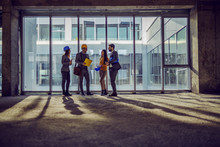 Four Dedicated Hardworking Architects Standing Next To Big Window In And Old Building And Talking About How They Plan To Rebuilt It To Be Modern.