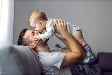 Wall Mural - Adorable little blond boy playing with his caring father and biting his nose. Father is smiling.