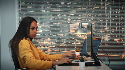 Side view of black female videographer working with footage and sound on computer with two displays and mounting video from different frames