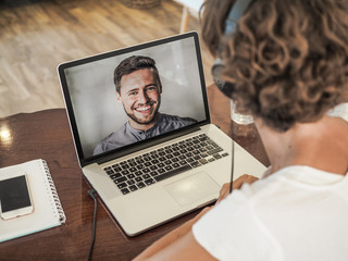 woman having a video conference call with a man on her laptop wearing a headset with notepad and mobile phone on the desk in her home office