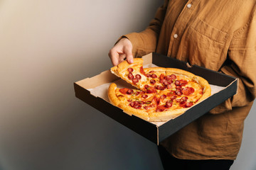 The female hand takes the first new piece of pepperoni pizza out of the delivery box. The concept of fast food