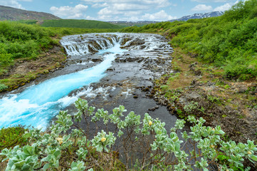 The beautiful and amazing bruarfoss waterfall in Iceland, the turquoise water stream. Green trees and blue skies in summer Here is a hidden waterfall in a secret place.