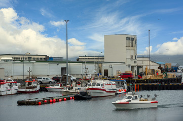 Harbor of factories and warehouses in Icelandic countryside There are many boats mooring at the pier on a beautiful sky day.