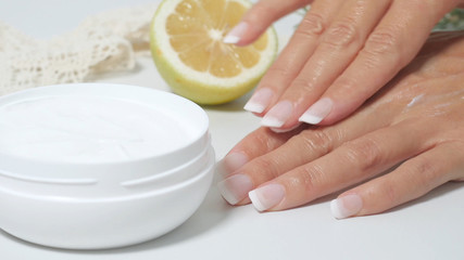  natural skin care, applying natural white cream on hands. Moisturizing treatment skin with natural ingredients. Cream, lemon, officinal herbs.