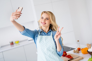 Photo of beautiful housewife hold telephone making selfie show v-sign symbol recording video vlog blog cooking tasty vegan meal quarantine stay home time kitchen indoors