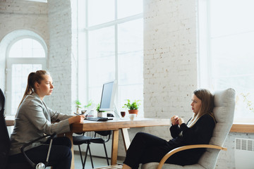 Wall Mural - Young woman sitting in office during the job interview with female employee, boss or HR-manager, talking, thinking, looks confident. Concept of work, getting job, business, finance, communication.