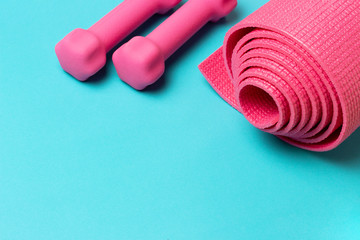 Sports mat and pink dumbbells on blue background, copy space