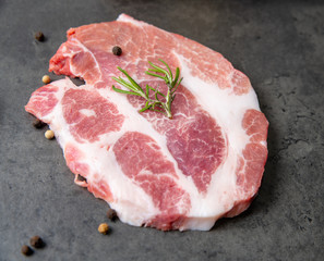 piece of meat on a gray cement background with rosemary and black pepper