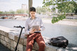 © Synergic Works OÜ - Serious man sitting on stone fence and looking at tablet. Freelancer man using tablet while sitting on stone fence next to scooter with river in background.