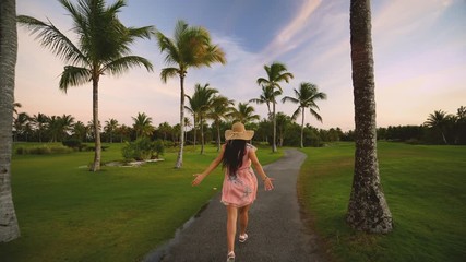 Wall Mural - Follow me concept of young woman running on tropical golf course path. Summer vacation or holiday