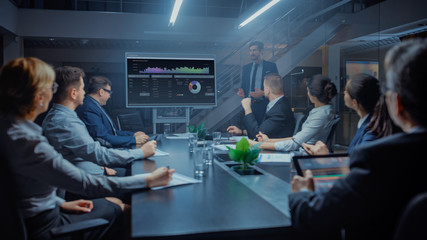 Wall Mural - In the Corporate Meeting Room: Male Executive Talks and Uses Digital Interactive Whiteboard for Presentation to a Board of Directors, Investors. Screen Shows Growth Data. Late at Night Office