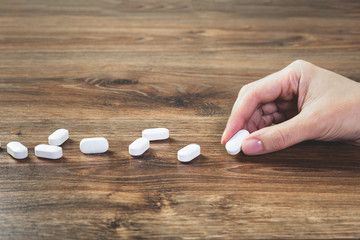 Wall Mural - Hand with white tablets pills lined on wooden table. Pharmacy. Healthcare and medicine concept drugs safety consumption or misuse with copy space. Medication