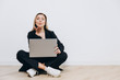 © Ulia - A beautiful young woman is sitting on the floor with a notebook pc on her lap, against a light background