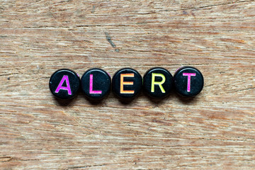 Poster - Black bead with color letter in word alert on wood background