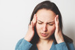 © mikhail_b_azarov - Portrait of a European young woman holding her hands to her temples with a severe headache. On light background.