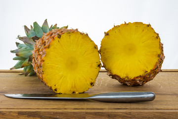 Fresh pineapple cut in half on cuttig board with knife.