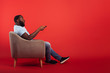 © alphaspirit - Televiewer on home chair changes channel with remote control on red background